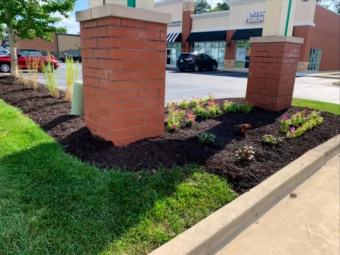 A brick pillar in the middle of a flower bed.