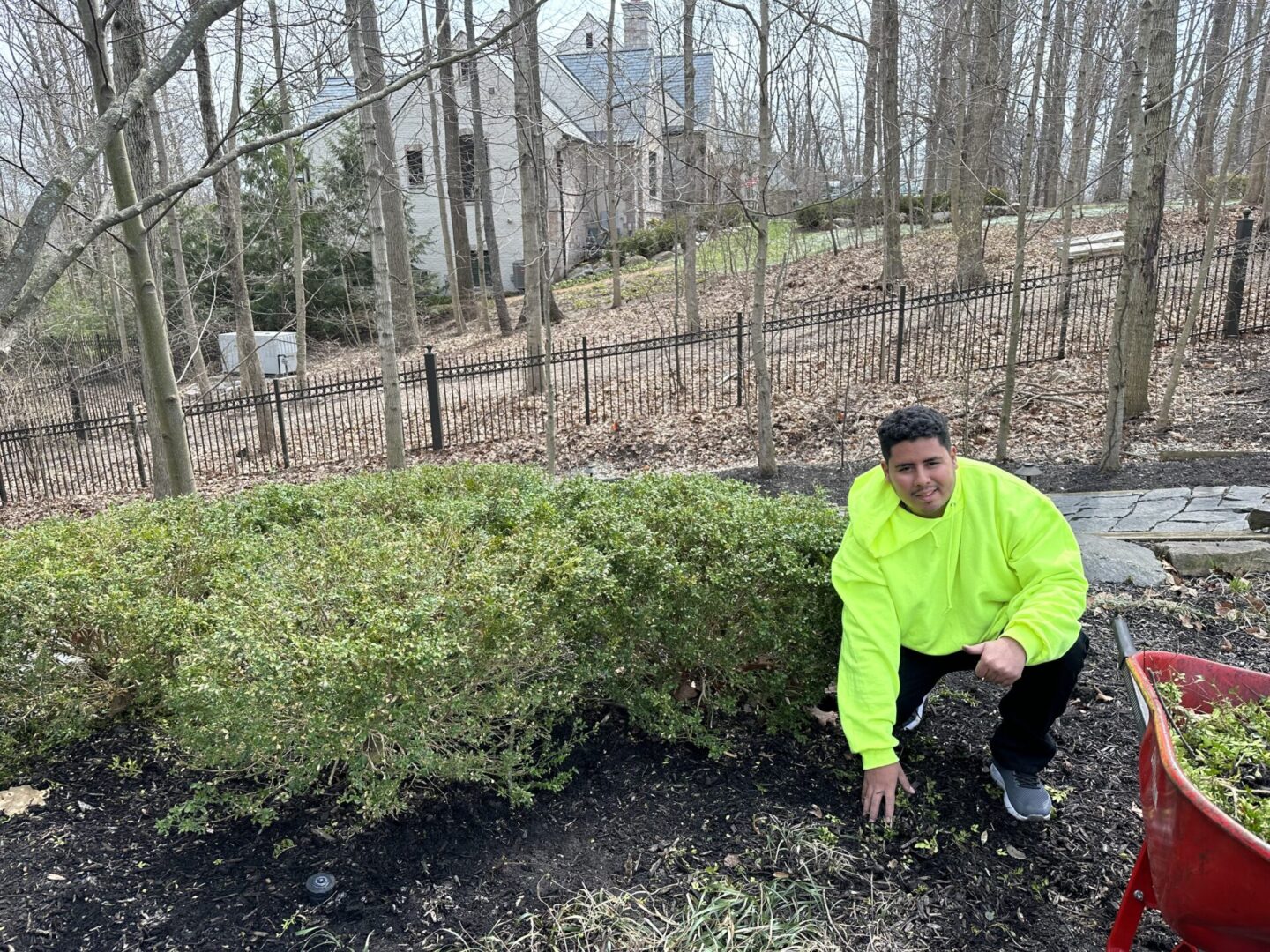 A man in yellow jacket squatting next to bushes.