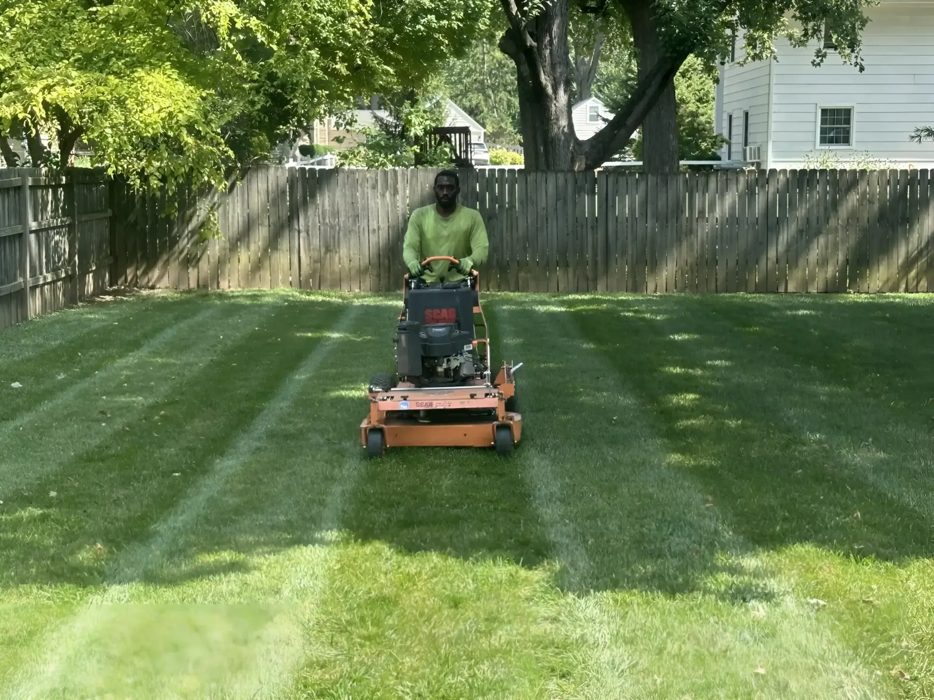 Person mowing striped backyard with riding mower