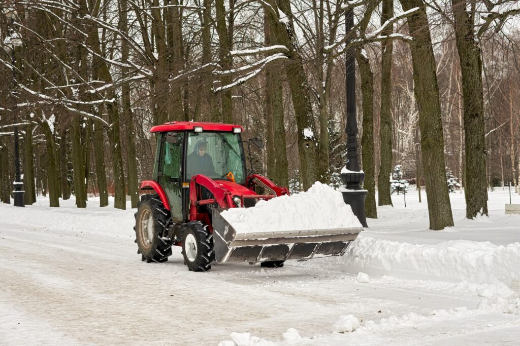 Red tractor clearing snow on park pathway
