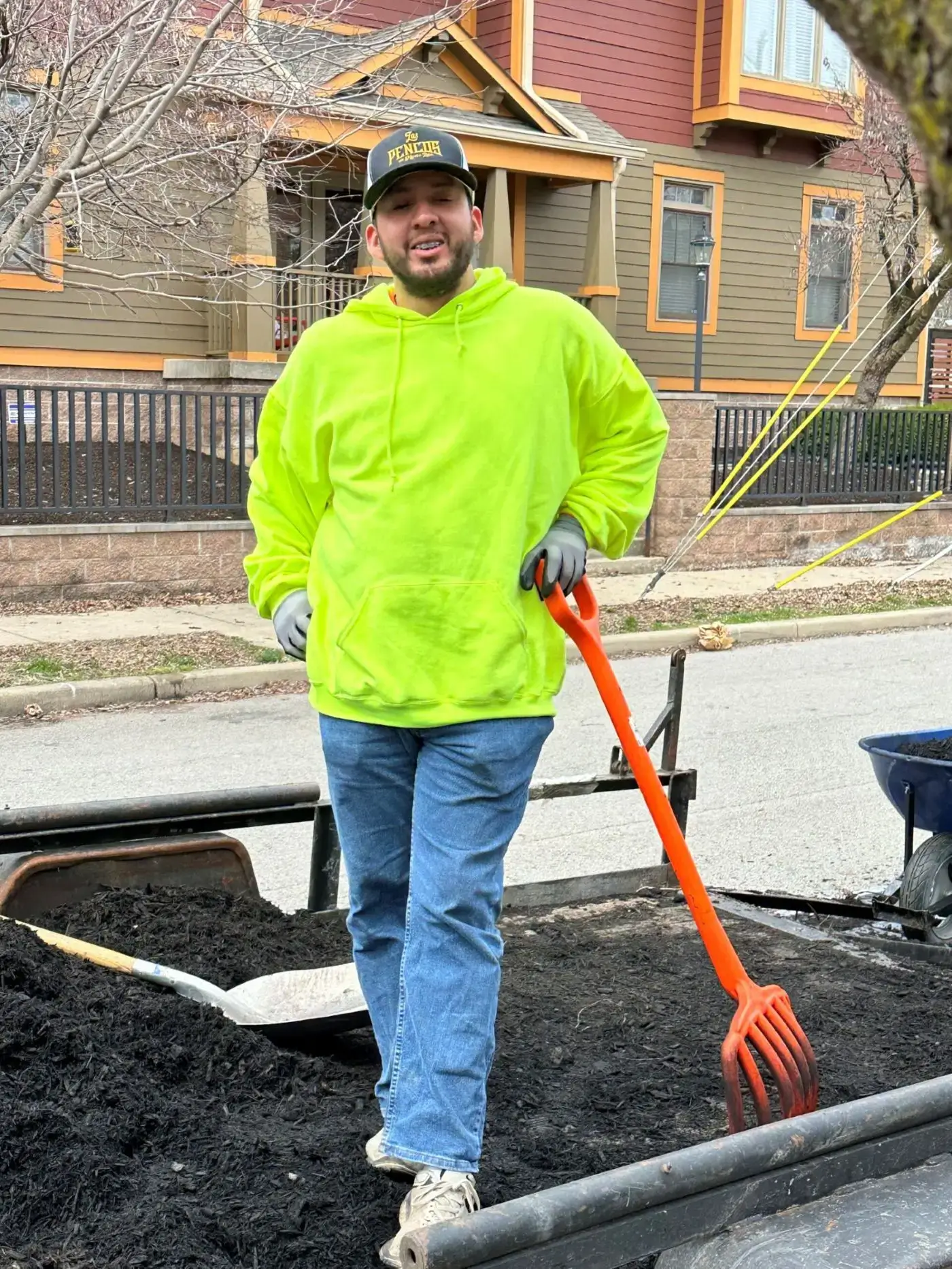 Smiling landscaper in neon hoodie holding orange rake